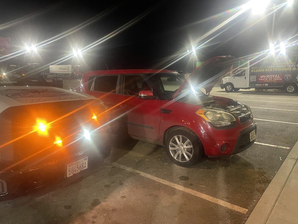 Red Kia Soul car with hood up, next to tow truck, parked at night.