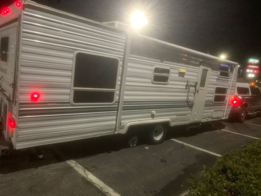 Gray and white camper trailer parked in a lot at night, lights on.