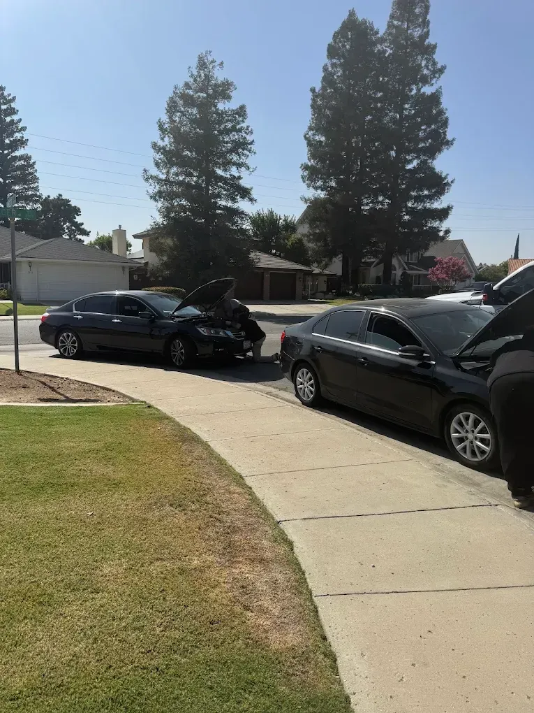 Two black cars involved in a collision on a residential street. One car's hood is open and damaged.