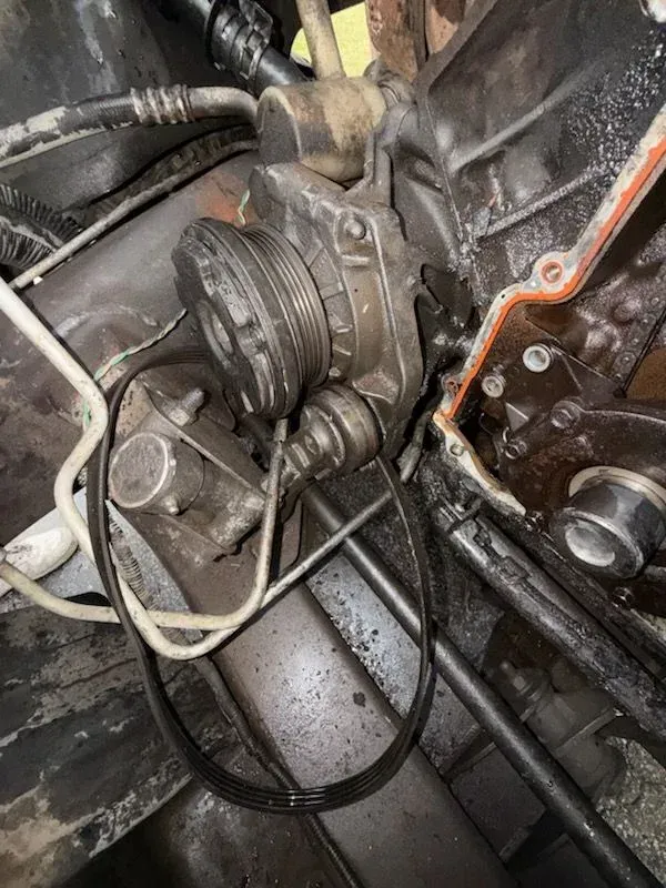 Engine compartment with a pulley, belt, and wires coated in oil.