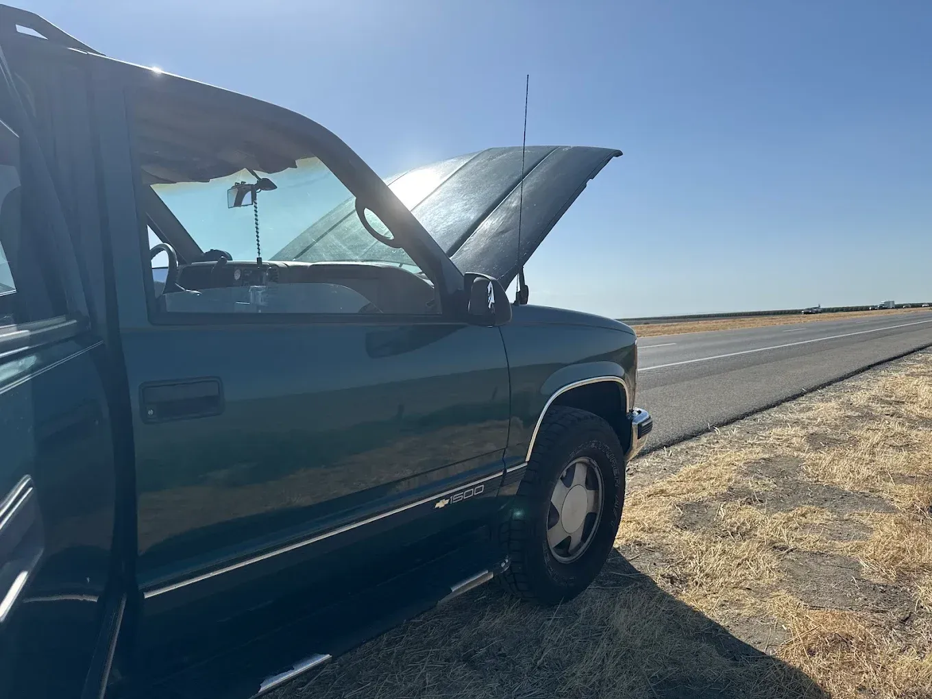 Green truck with hood open, parked on side of a sunny road.