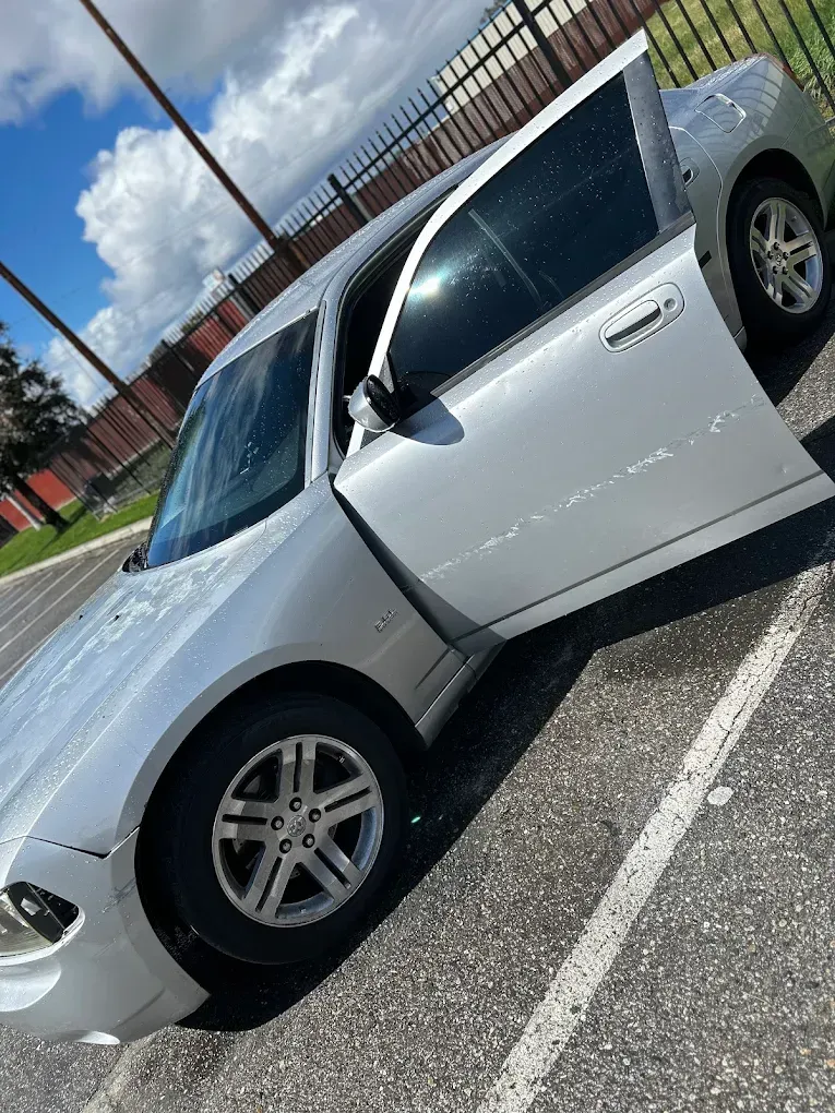 Silver Dodge Charger with the driver's side door open, parked on asphalt. Cloudy sky in background.