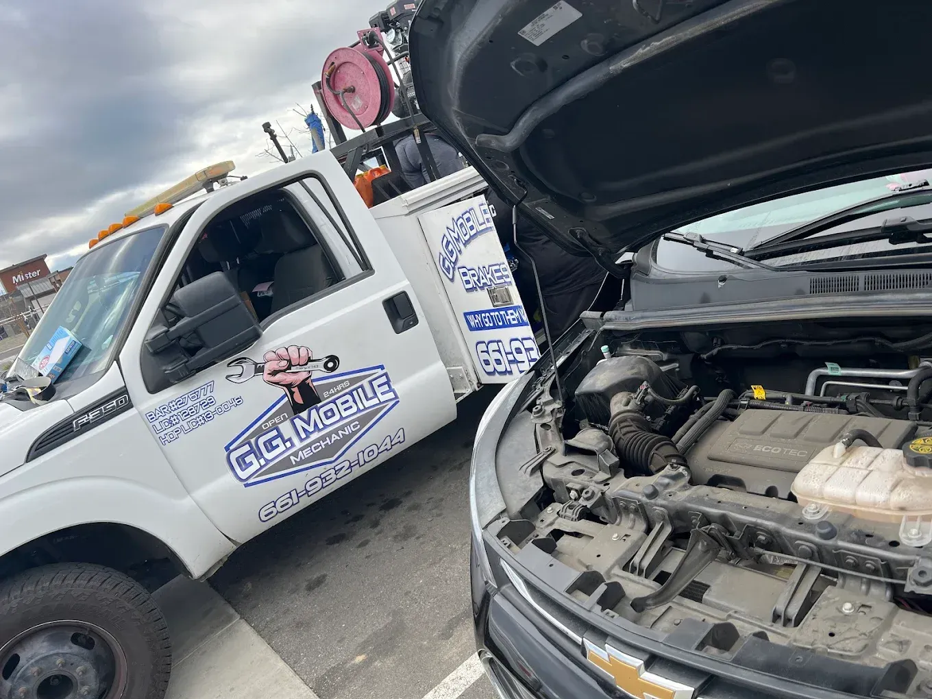 Tow truck parked next to a car with an open hood, on an overcast day.