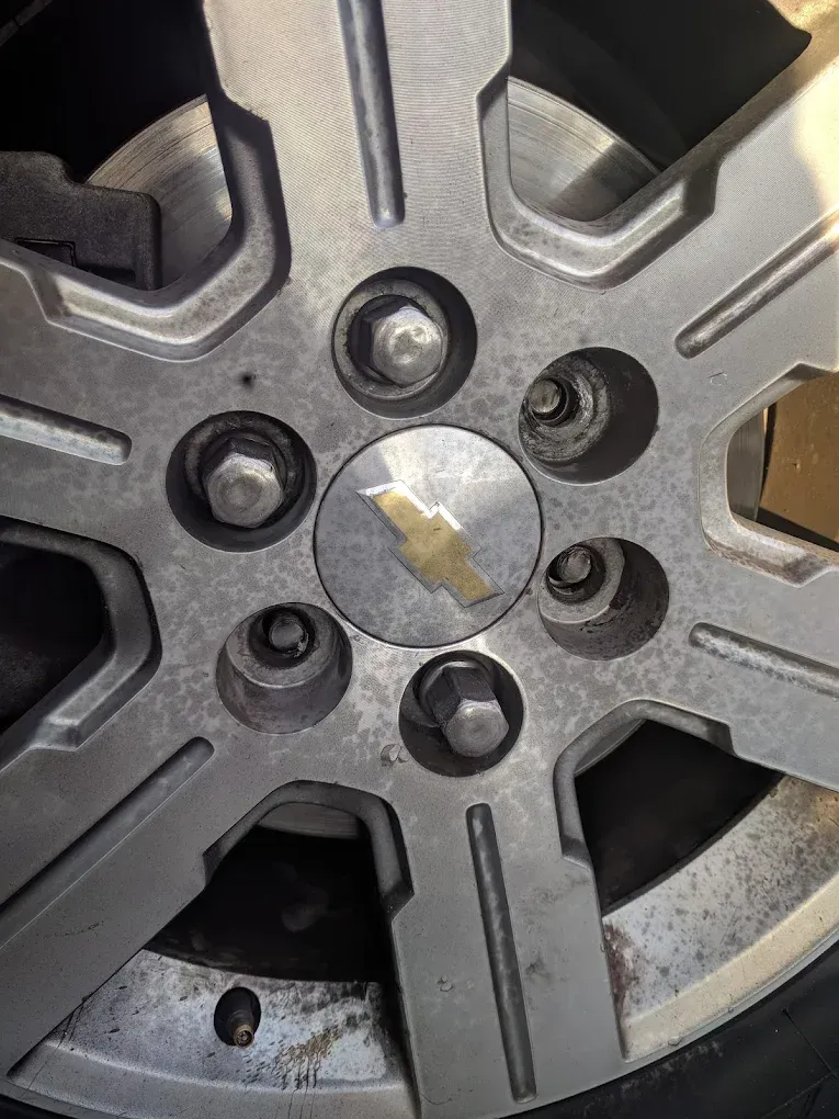 Silver Chevrolet car wheel with lug nuts and emblem.