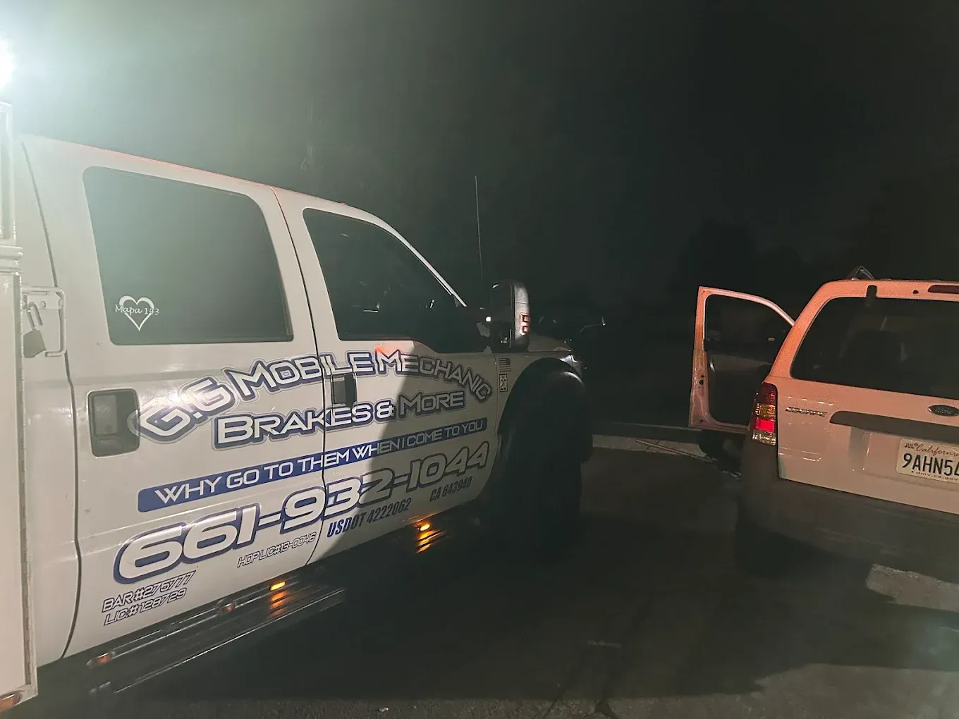 White service truck with logo and phone number next to a white SUV at night.