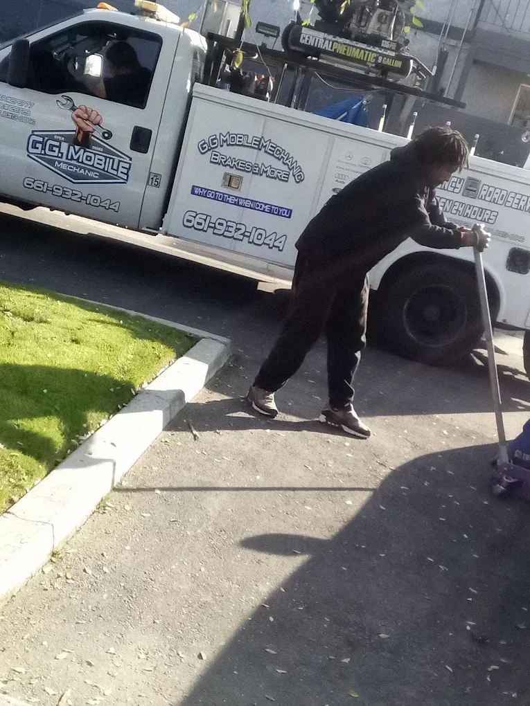 Person using a jack near a tow truck. The tow truck is white, parked near grass and asphalt.