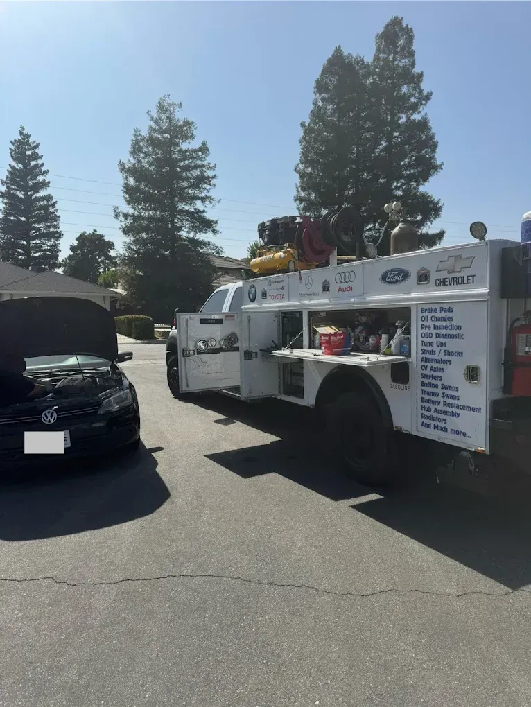 A black car with open hood next to a white service truck with open side doors.