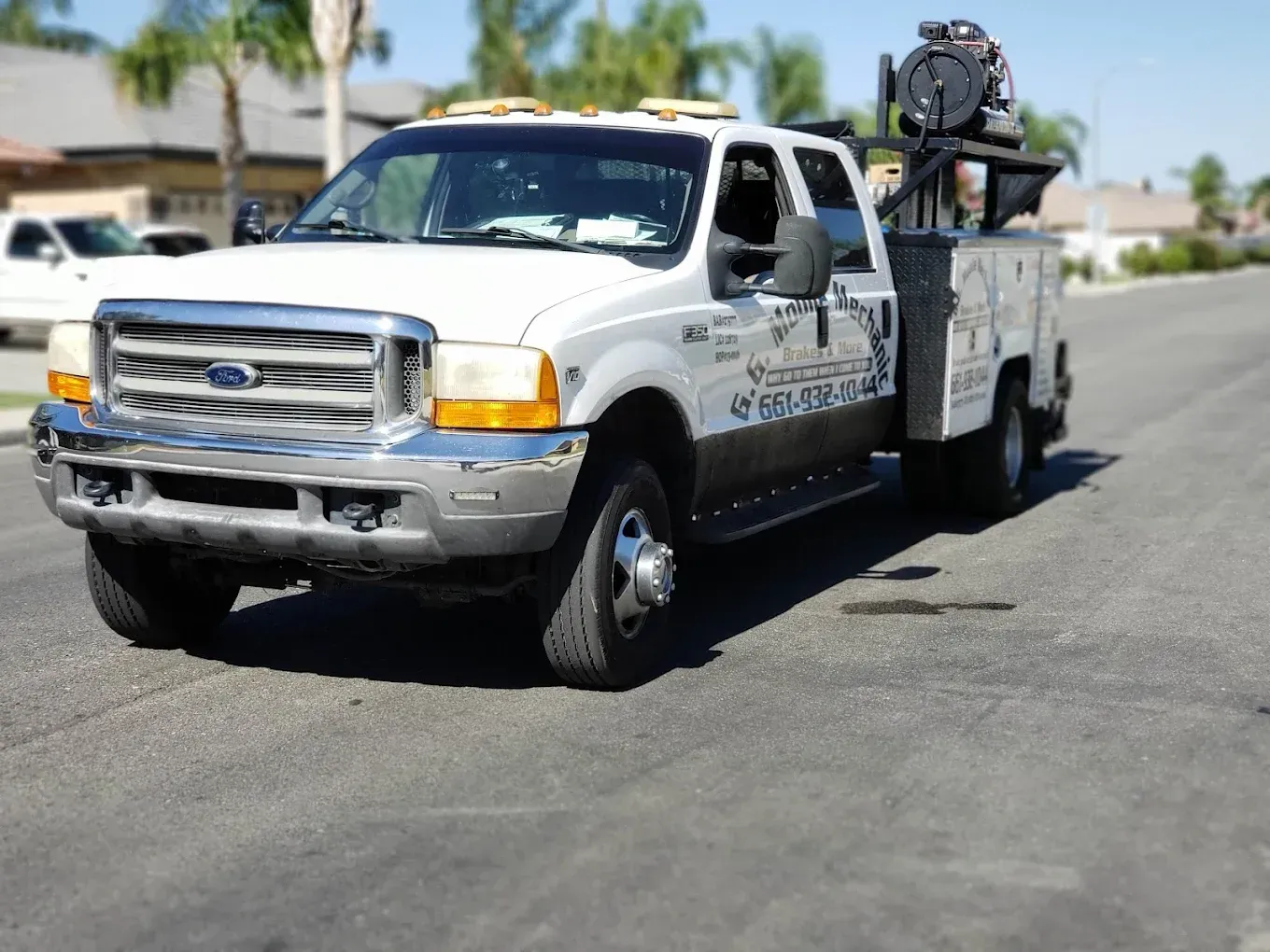 White work truck parked on a residential street. The truck has a utility bed and equipment on top.