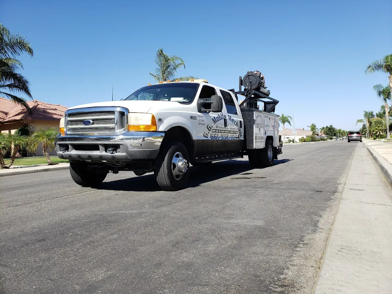White work truck on a street, with equipment on its bed. Bright sunny day, houses in background.
