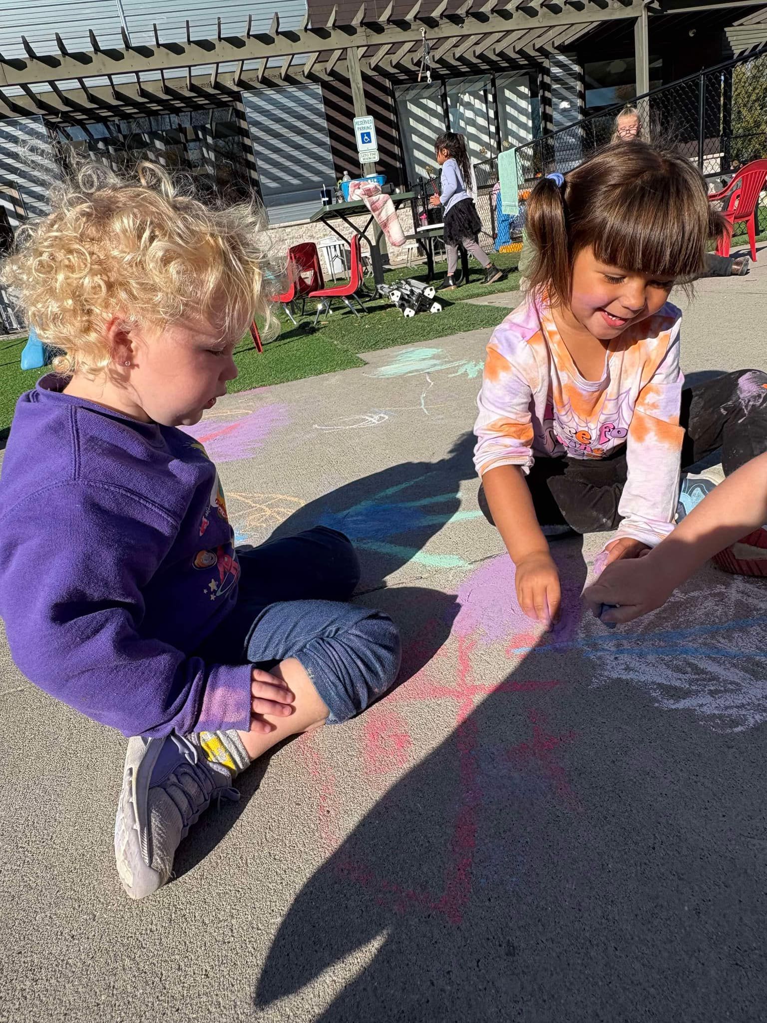 Two children drawing with chalk on pavement outside.