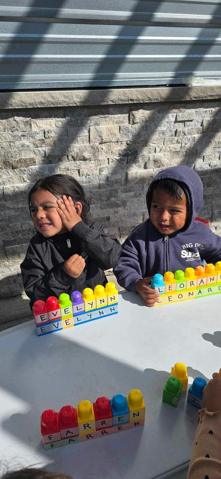 Two children playing with colorful building blocks on a white table outdoors.