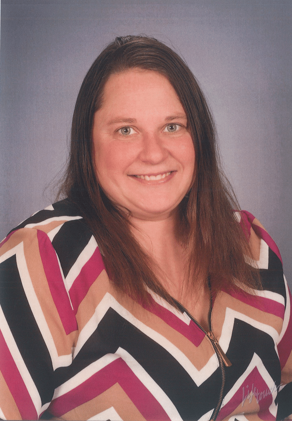 Woman smiling in front of a blue background, wearing a patterned zig-zag top.