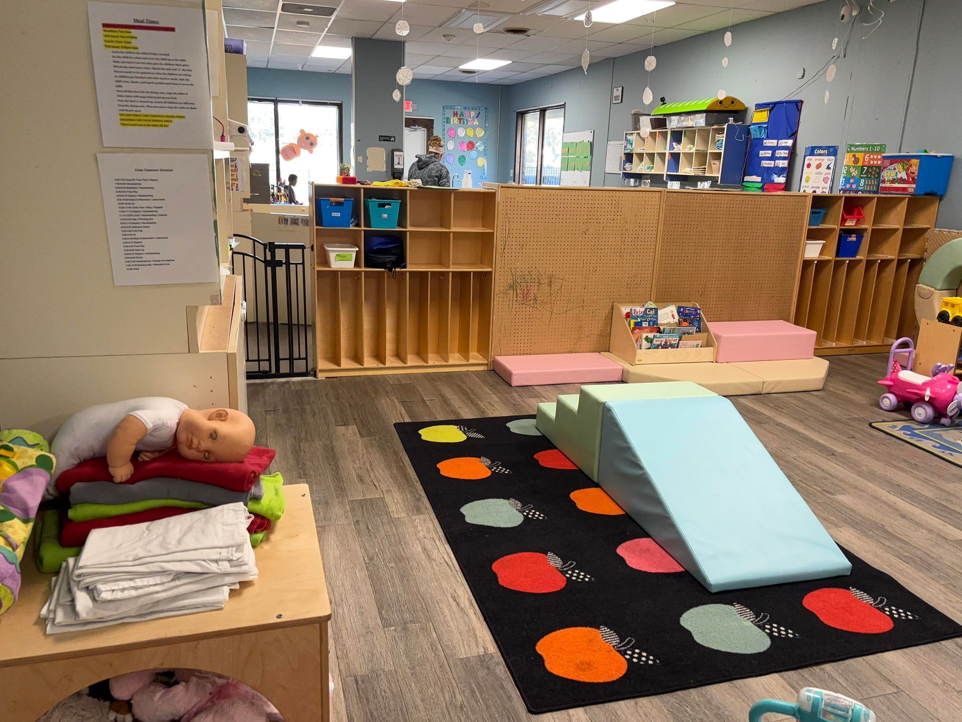Childcare room with play area, books, and storage. Includes a ramp and colorful rug.