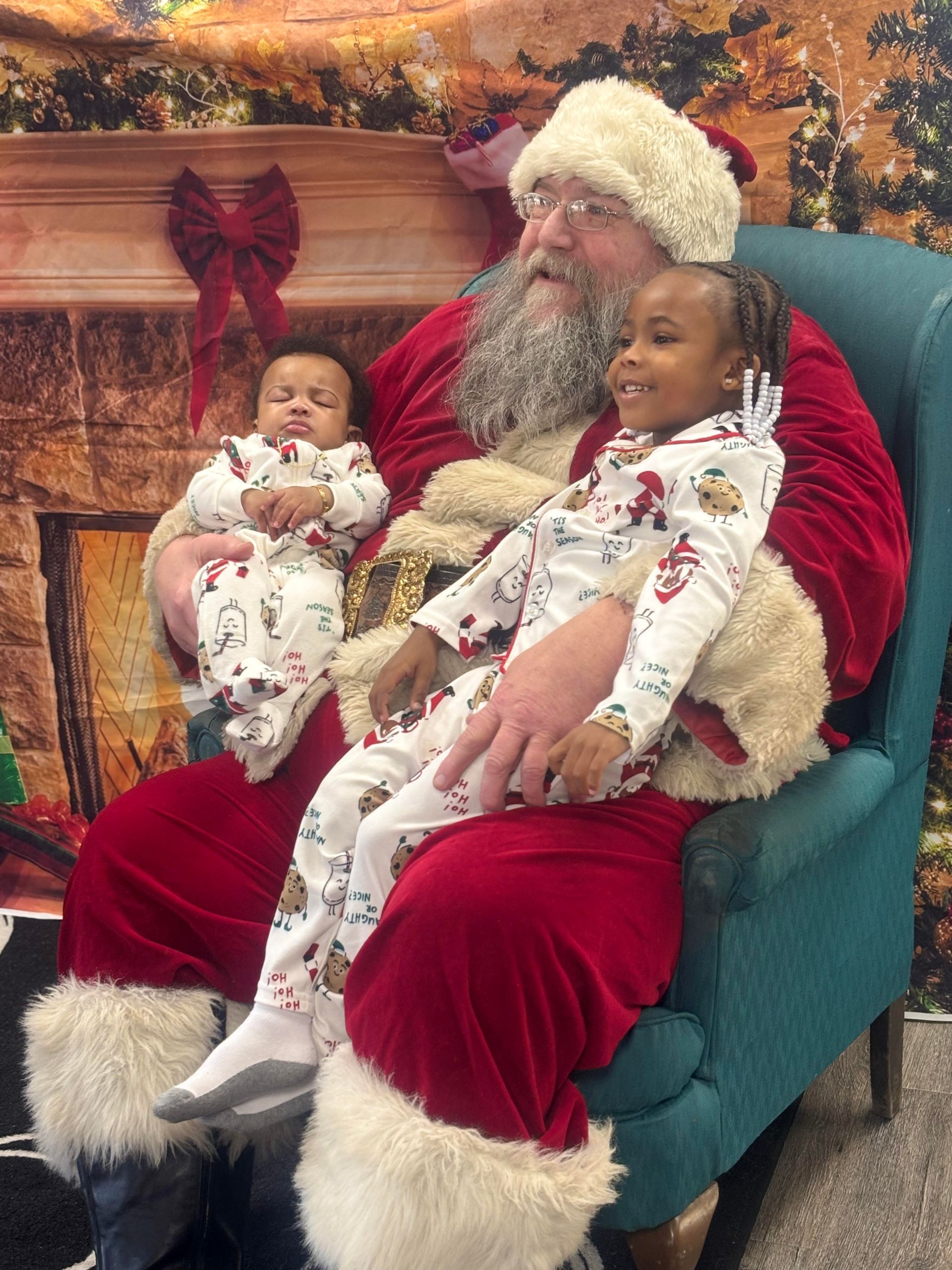 Santa Claus sits with two children in matching pajamas.