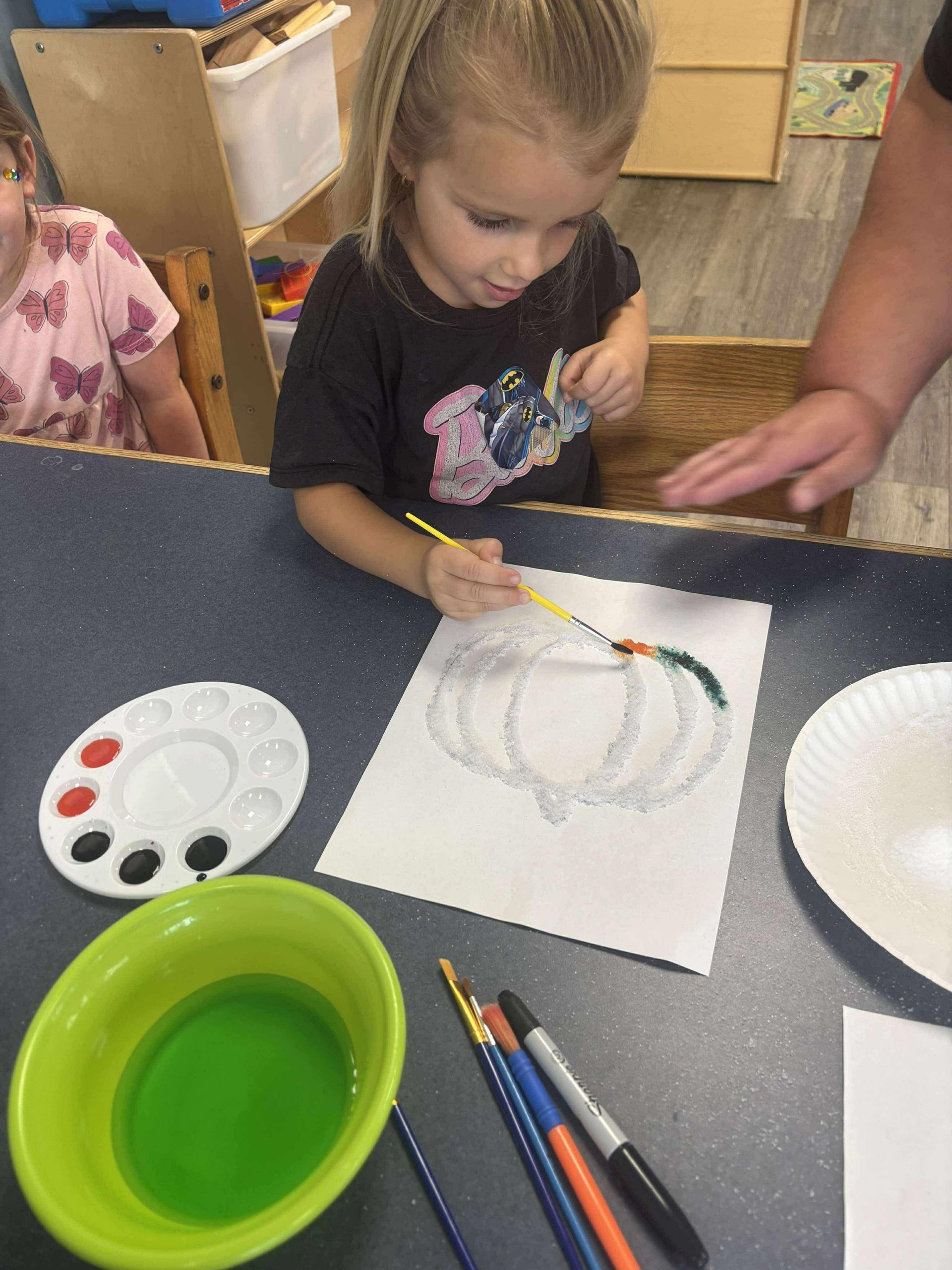 Girl paints a pumpkin outline with a paintbrush and paints in a classroom.