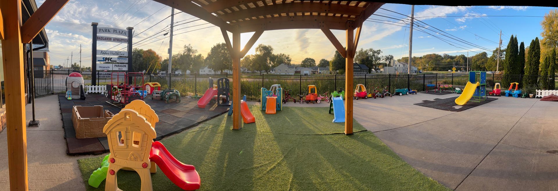 A playground with slides, play structures, and a wooden pergola, under a blue sky.