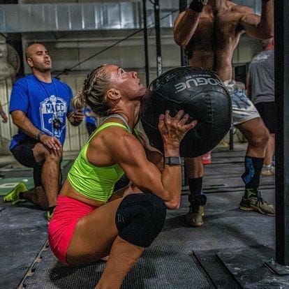 A woman is squatting down while holding a medicine ball in a gym.
