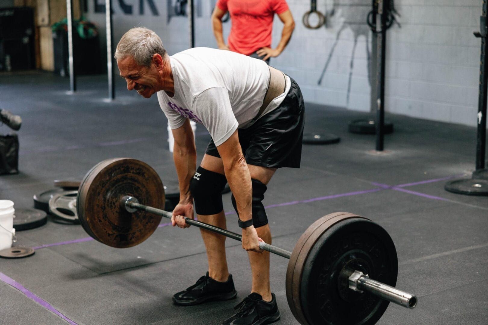 A man is lifting a barbell in a gym.