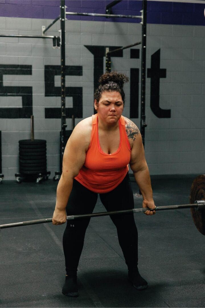 A woman is lifting a barbell in front of a sign that says crossfit