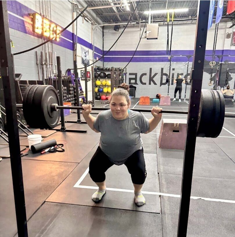 A woman squatting with a barbell in front of a sign that says blackbird