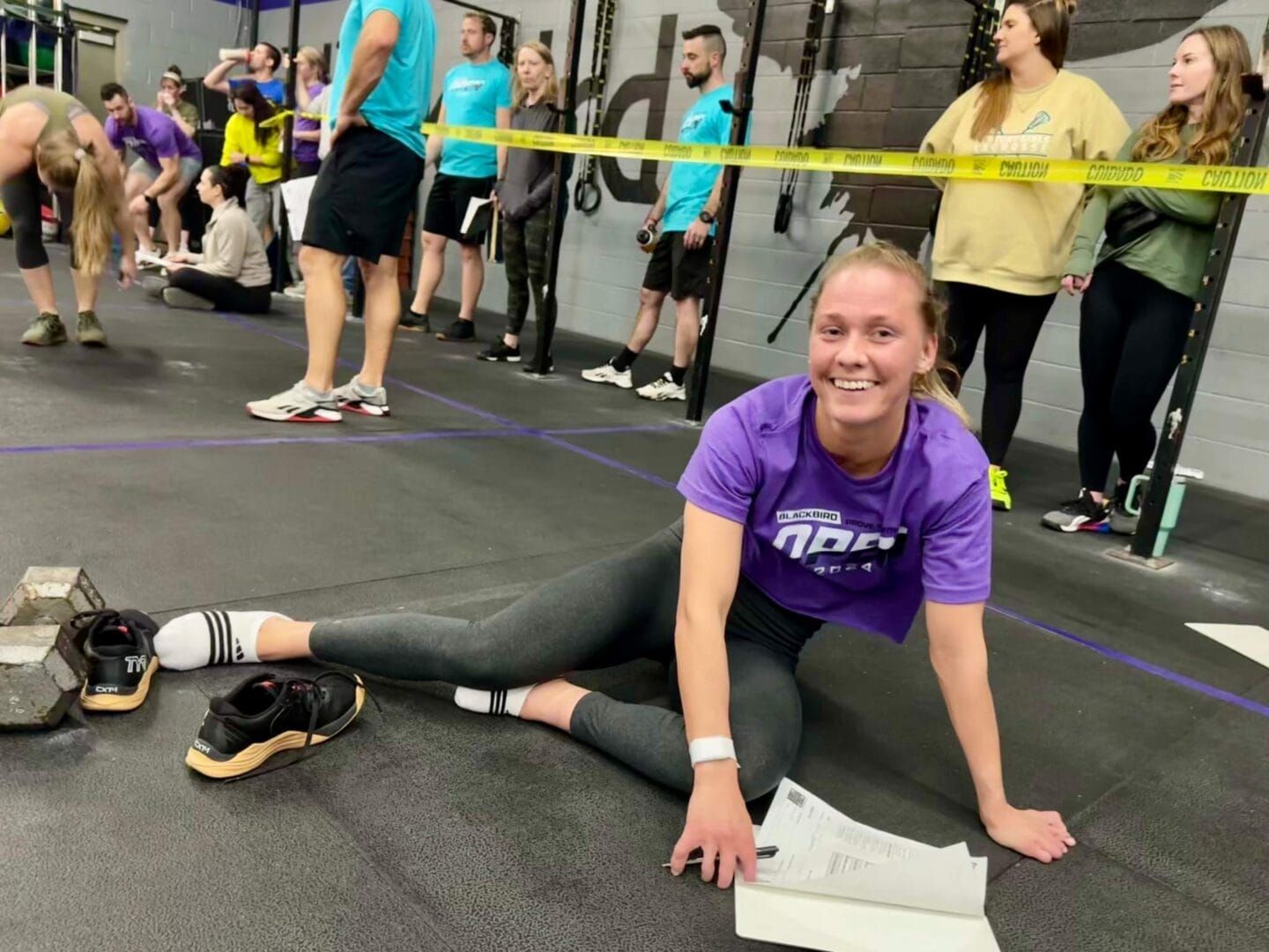 A woman in a purple shirt is sitting on the floor in a gym.