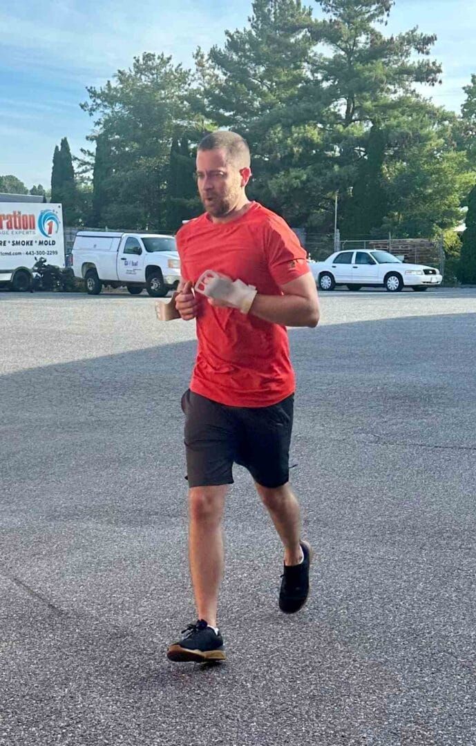 A man in a red shirt and black shorts is running in a parking lot.