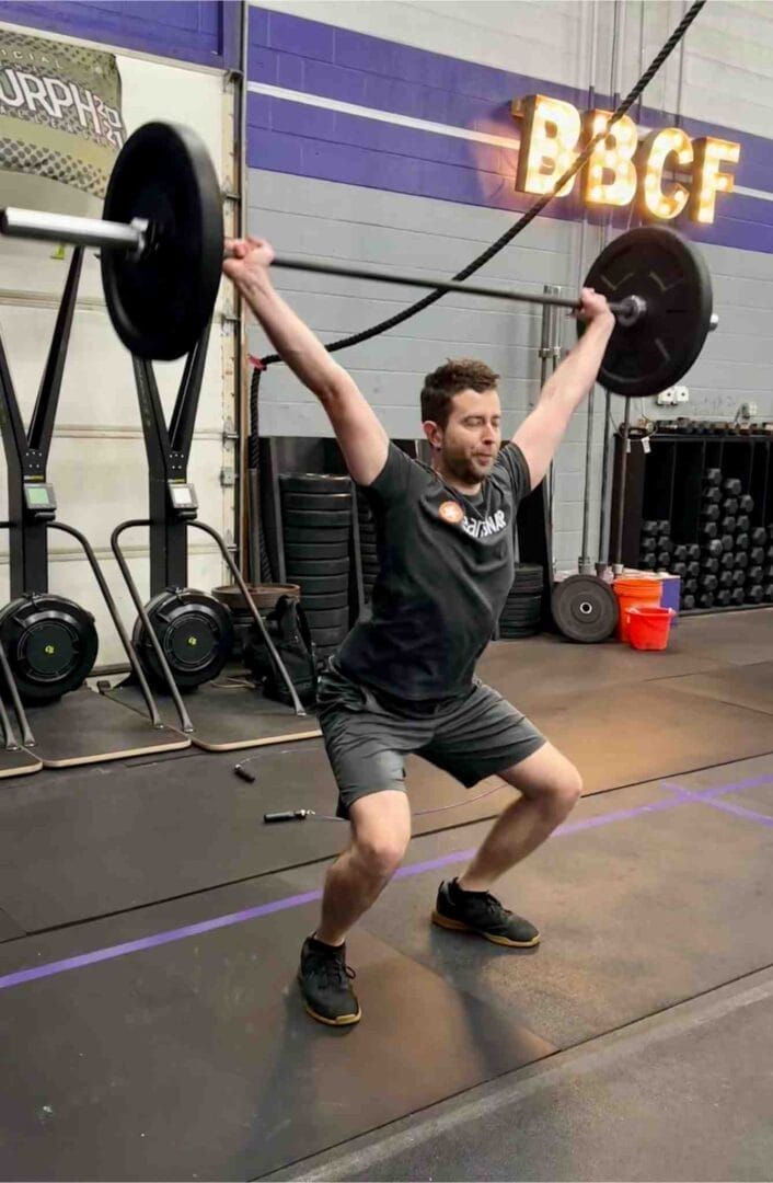 A man is squatting down while lifting a barbell in a gym.