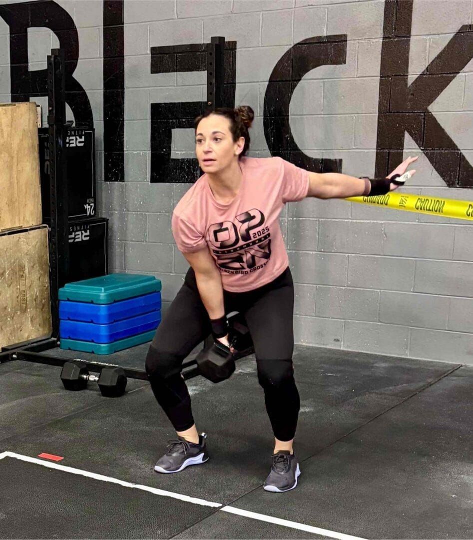 A woman is squatting with a dumbbell in a gym.