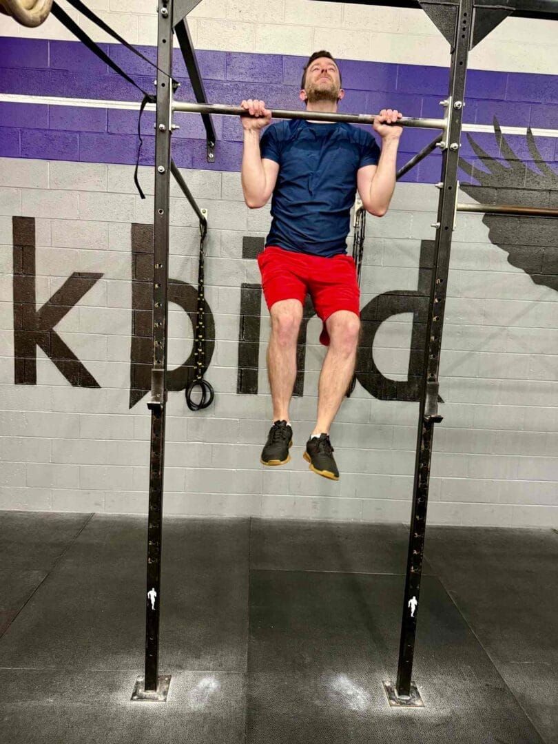 A man is doing a pull up on a bar in a gym.