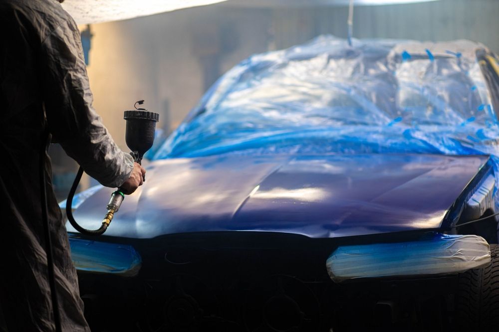 A Man is Spray Painting a Purple Car in a Garage — Sure Shot Sprayer Australia in Alice Springs, NT