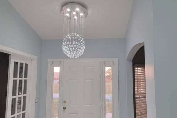 A bright foyer featuring a modern crystal ball chandelier hanging above a white front door with glass sidelights.
