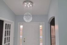 A bright foyer featuring a modern crystal ball chandelier hanging above a white front door with glass sidelights.