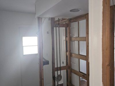 A partially renovated room featuring exposed wooden wall framing, a soffit with a recessed light, and a bright window.
