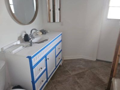A white bathroom vanity with a round mirror, blue painter’s tape applied to its edges, and a sink on top.