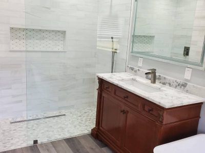 A bright bathroom featuring a walk-in glass shower, a marble-topped wooden vanity, and a large wall mirror.