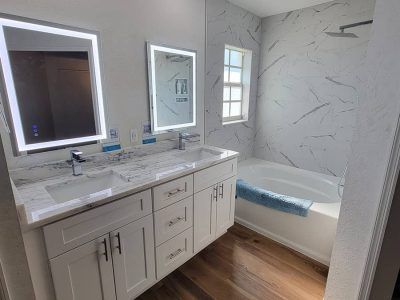 A modern bathroom with a double vanity, marble-patterned backsplash, two illuminated mirrors, and a soaking tub.