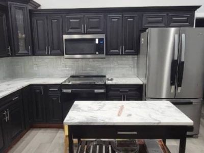 A kitchen featuring dark wood cabinets, a stainless steel microwave and refrigerator, white countertops, and an island.