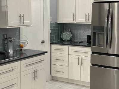 Modern kitchen with white shaker cabinets, dark countertops, blue-grey herringbone backsplash, and a stainless fridge.