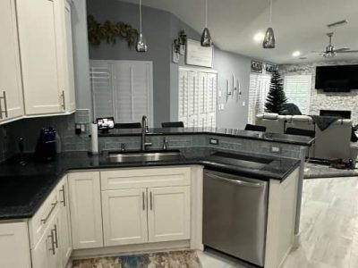 A kitchen with white cabinets, dark countertops, and stainless steel appliances, opening into a living room with a TV.