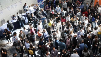 Large crowd of people gathered indoors, many wearing casual clothing, possibly at a conference or event.