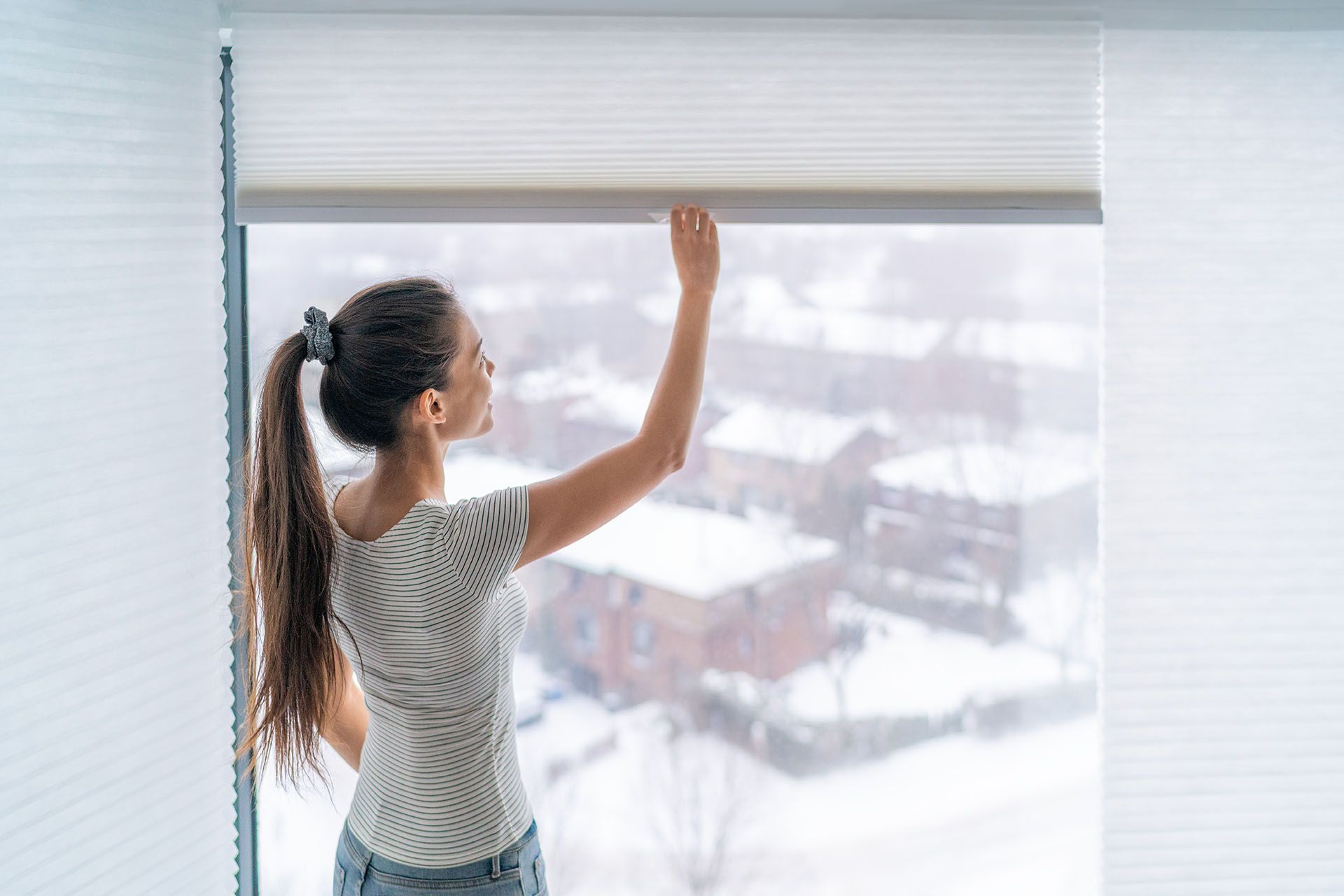 Woman opening windows shade blind during winter morning.
