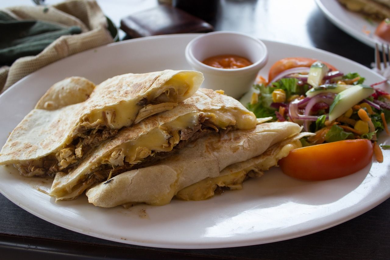 a white plate topped with quesadillas and vegetables on a table .