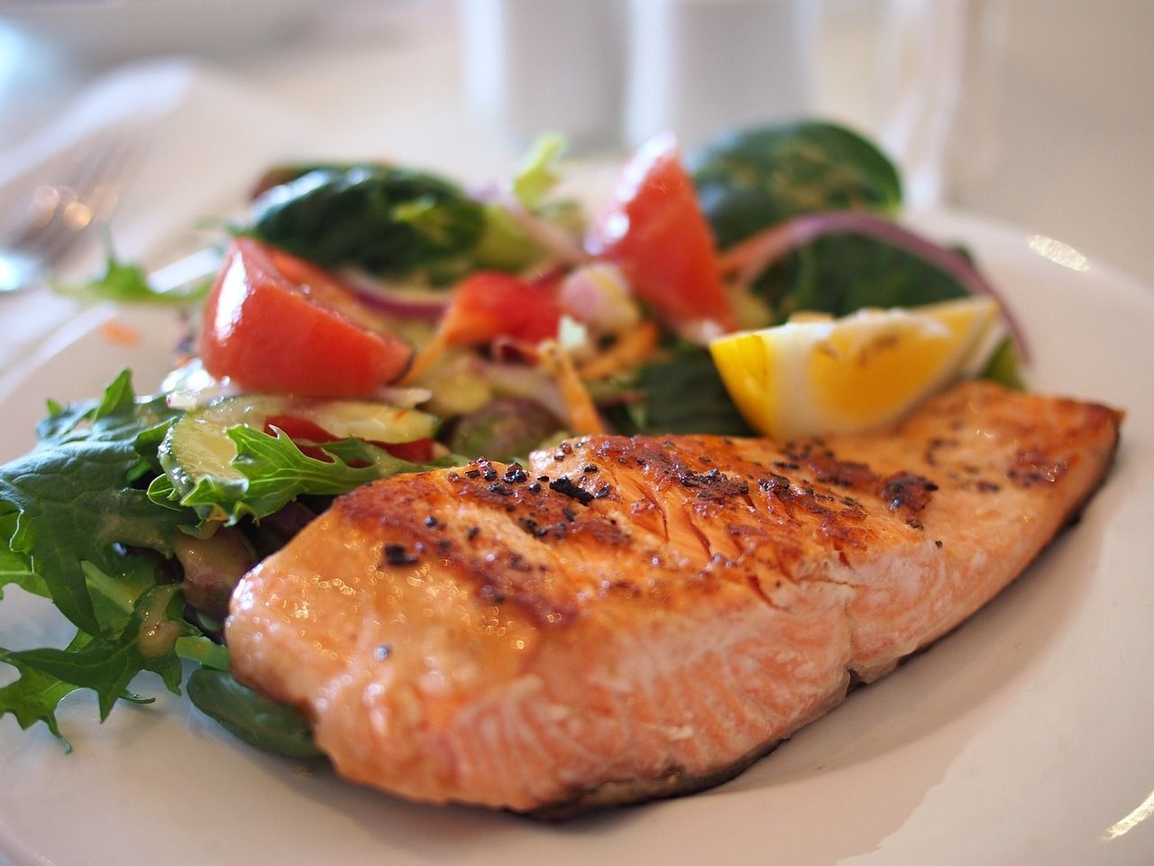 a white plate topped with a piece of salmon and a salad .