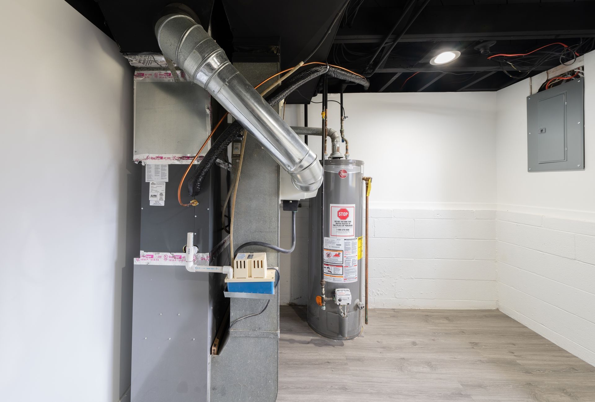 Basement with furnace, water heater, ductwork, electrical panel, and white walls.