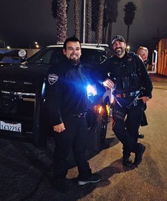 Two police officers are posing for a picture in front of a car