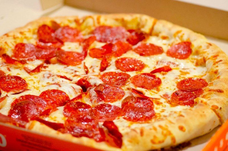 A pepperoni pizza is in a box on a table.
