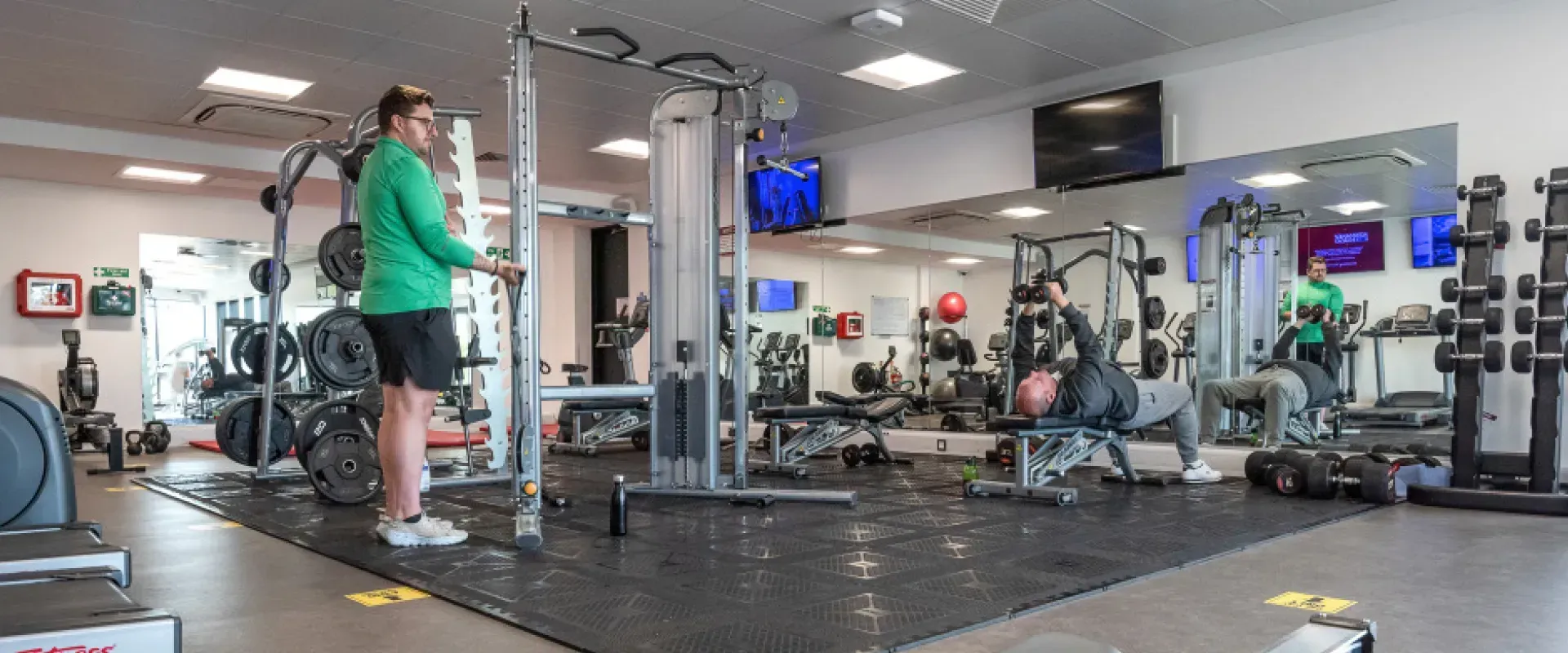 A man in a green jacket is standing in a gym.