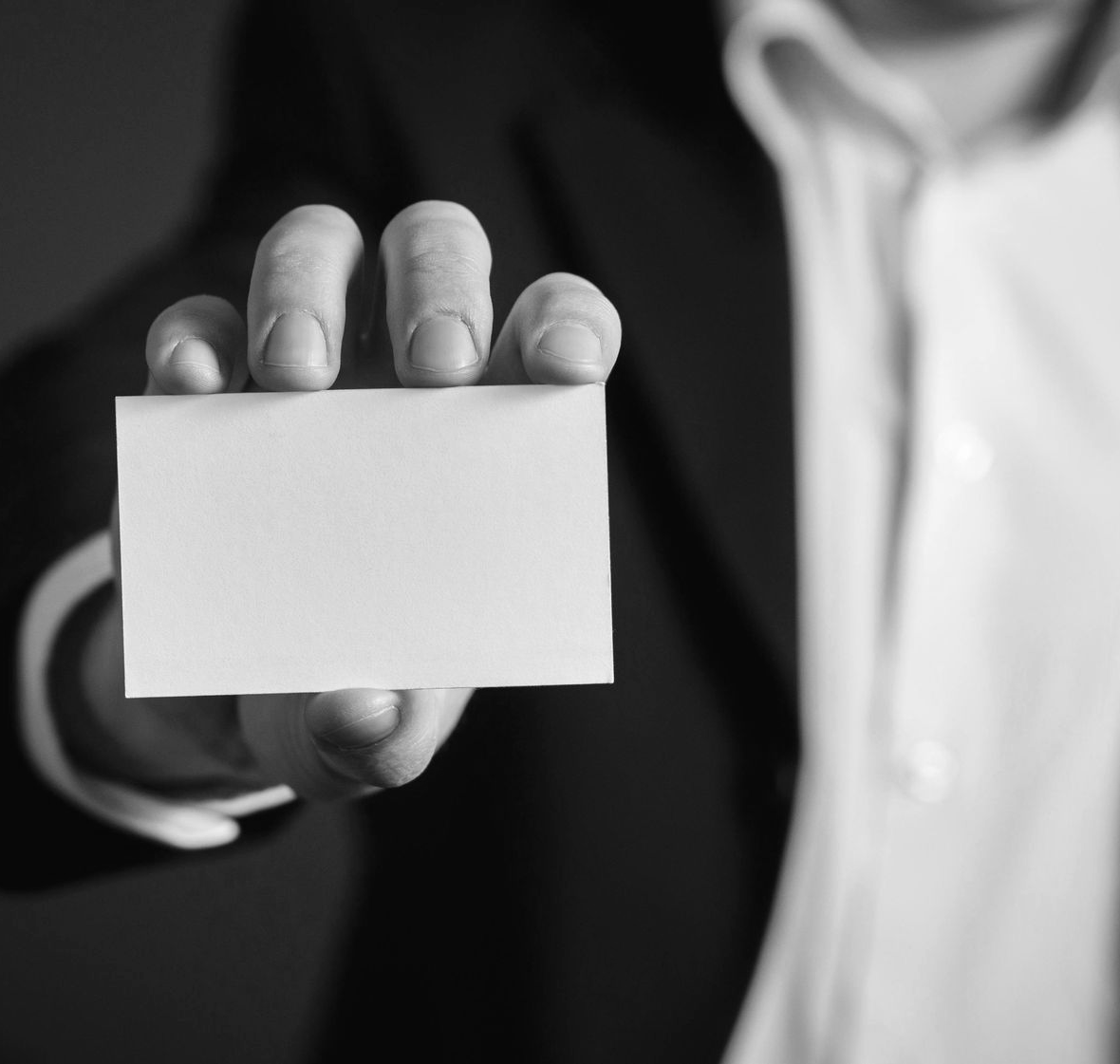 Person in suit holding a blank business card towards the viewer.