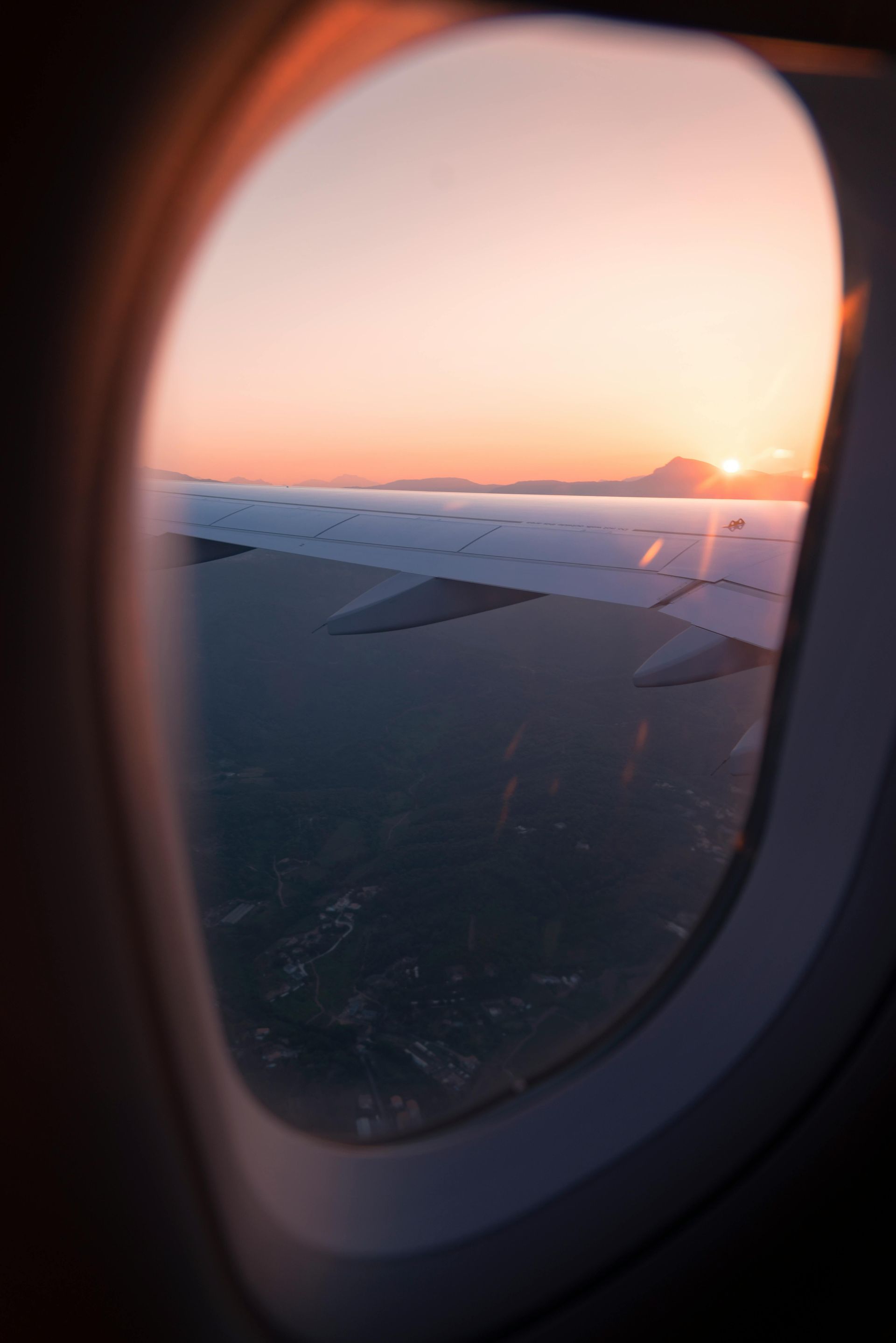 Sunset view from an airplane window, showing wing and fiery sky over land.