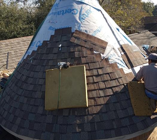 A man is sitting on a roof with a cone shaped roof covered in shingles